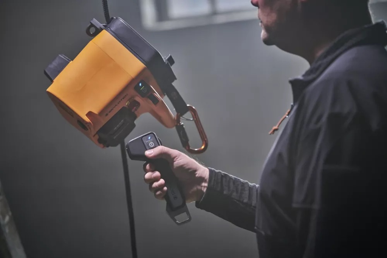 Mann hält eine orangefarbene elektrische Winde mit Fernbedienung in einem dunklen Raum.